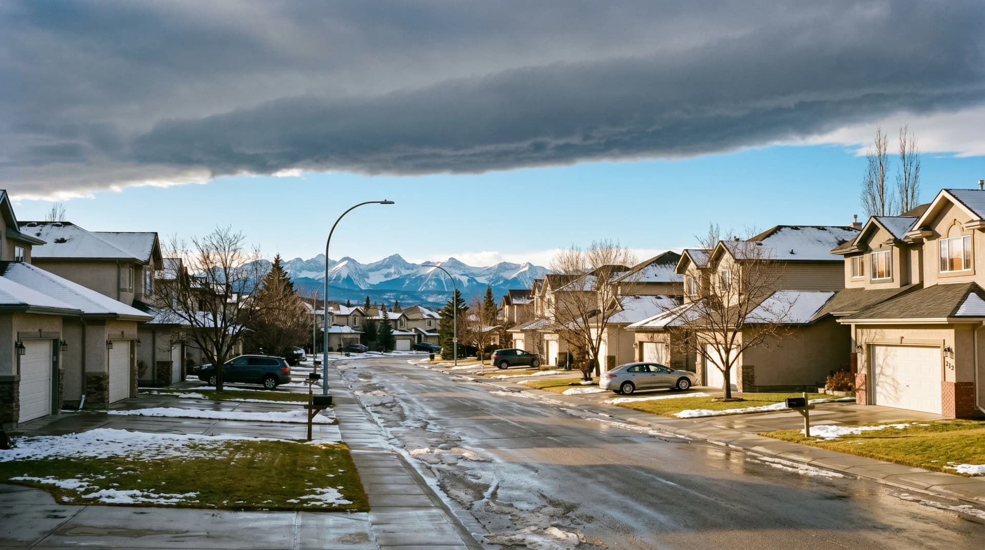 A Calgary residential street under a dramatic chinook arch cloud with patches of melting snow on green lawns and the Canadian Rockies on the horizon — the temperature swing Calgary homes endure